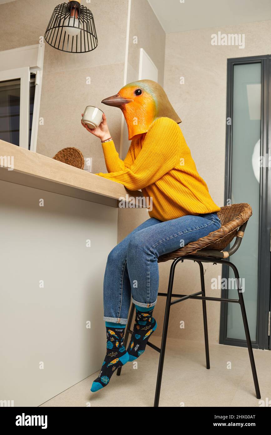 Une femme vêtue d'un masque d'oiseau boit une tasse de café dans la cuisine Banque D'Images