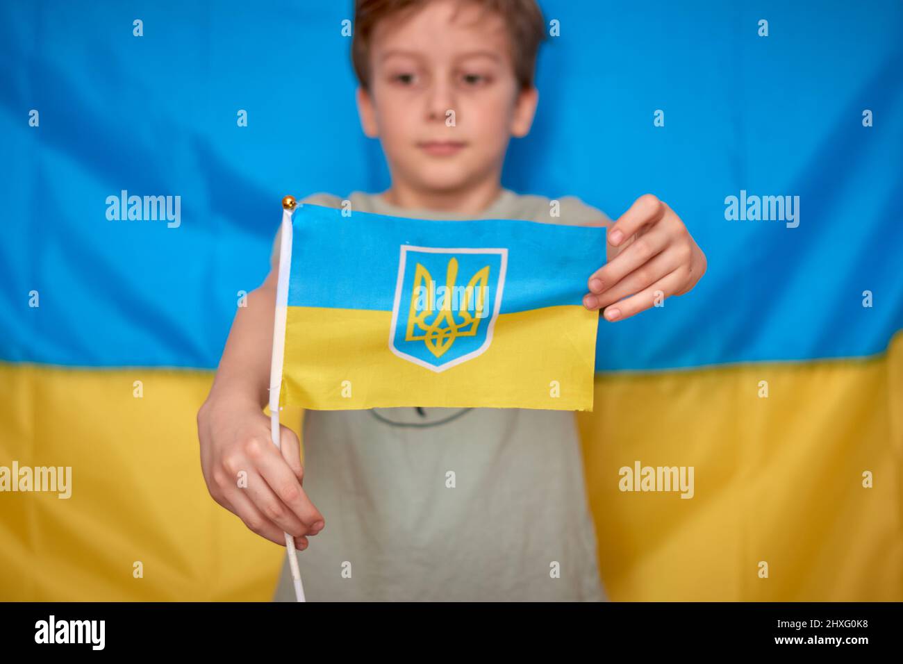 Garçon tenant entre les mains drapeau ukrainien sur fond jaune-bleu. Les enfants soutiennent l'Ukraine en montrant du cœur. Crise ukrainienne, agression russe en Ukraine. Guerre de la Russie contre l'Ukraine. Banque D'Images