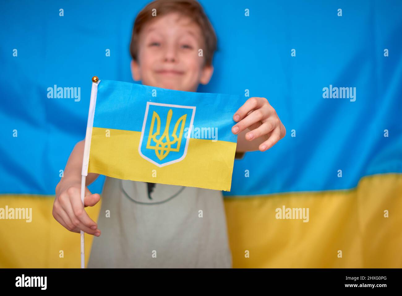 Garçon tenant entre les mains drapeau ukrainien sur fond jaune-bleu. Les enfants soutiennent l'Ukraine en montrant du cœur. Crise ukrainienne, agression russe en Ukraine. Guerre de la Russie contre l'Ukraine. Banque D'Images