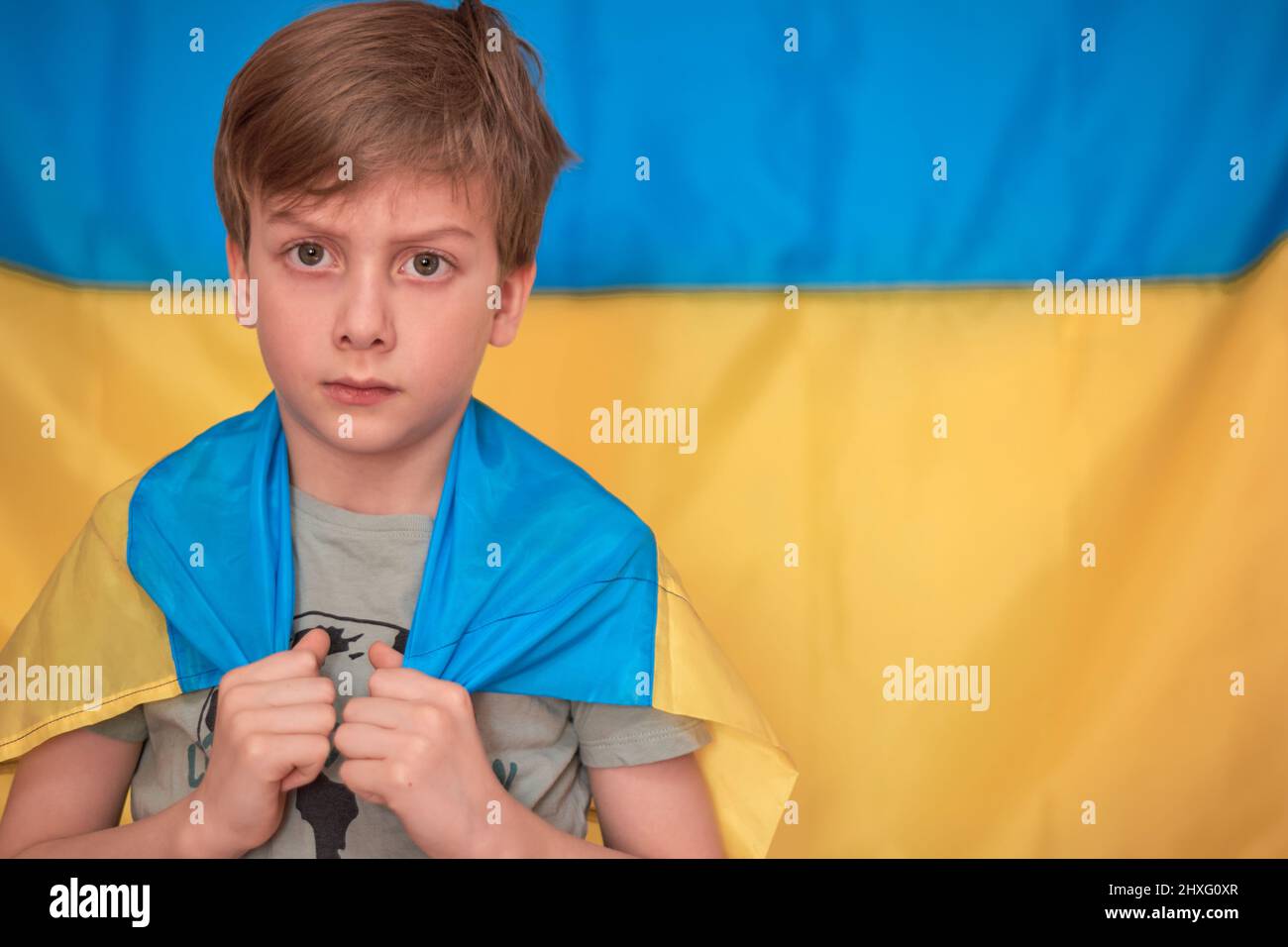 Garçon tenant entre les mains drapeau ukrainien sur fond jaune-bleu. Les enfants soutiennent l'Ukraine en montrant du cœur. Crise ukrainienne, agression russe en Ukraine. Guerre de la Russie contre l'Ukraine. Banque D'Images