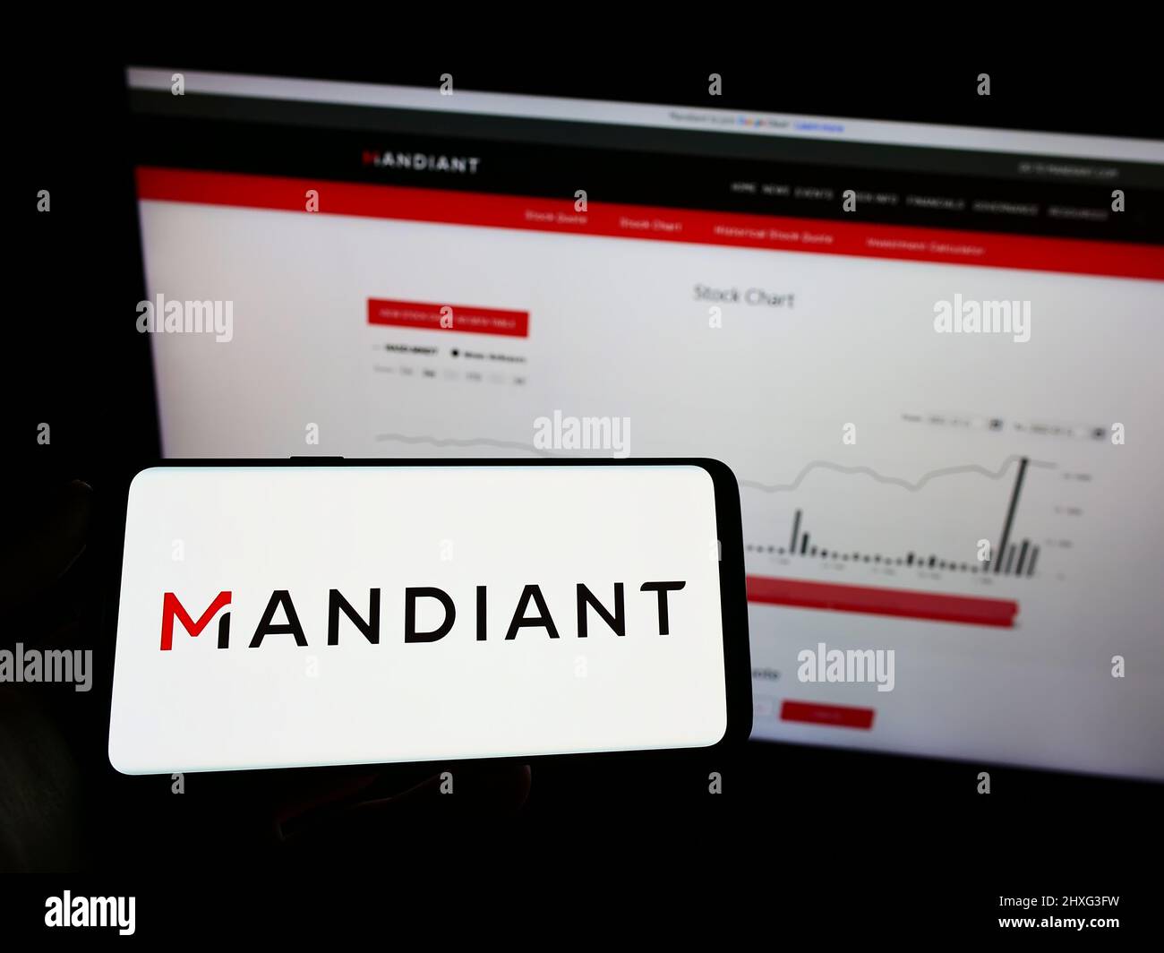 Personne portant un smartphone portant le logo de la société de cybersécurité américaine Mandiant Inc. À l'écran devant le site Web. Mise au point sur l'affichage du téléphone. Banque D'Images