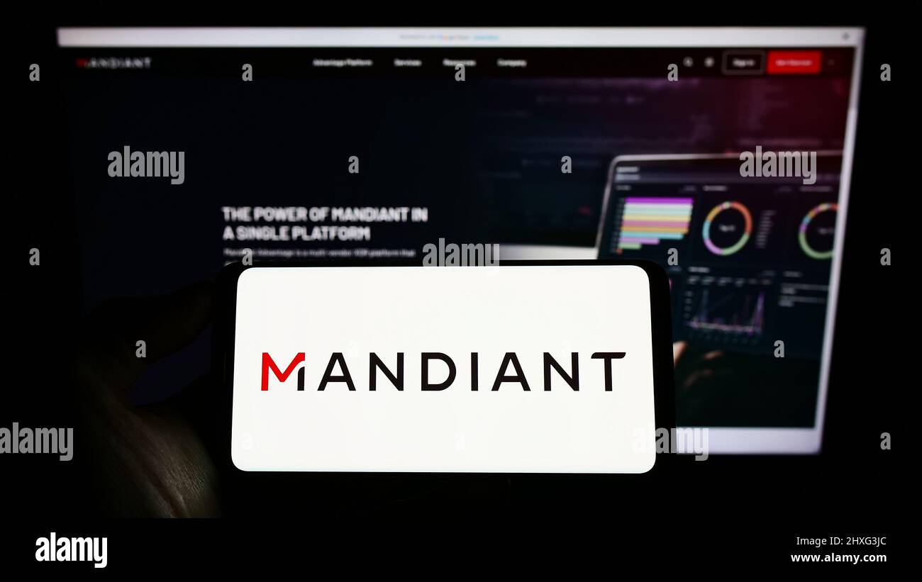 Personne tenant un téléphone portable avec le logo de la société de cybersécurité américaine Mandiant Inc. À l'écran devant la page Web des affaires. Mise au point sur l'affichage du téléphone. Banque D'Images