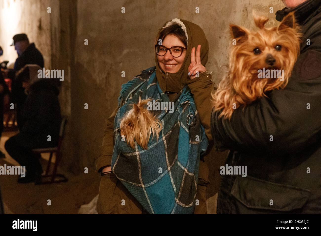UZHHOROD, UKRAINE - le 12 MARS 2022 - Une femme avec un Yorkshire Terrier dans une élingue faite d'une couverture montre un V-signe alors qu'elle reste dans un abri à la bombe après Banque D'Images