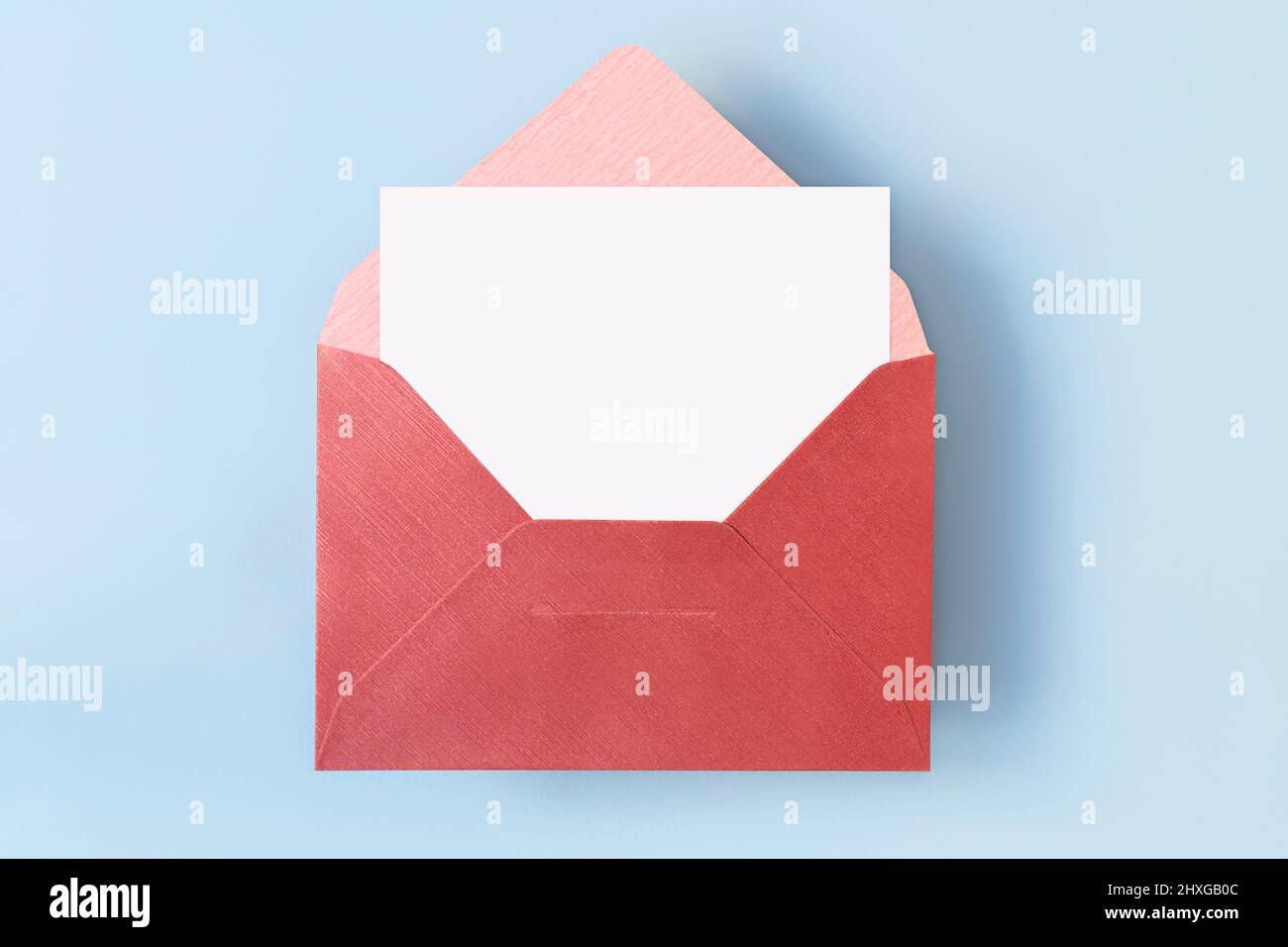 Vue de dessus de l'enveloppe rouge avec une carte blanche vierge vide sur fond bleu clair, espace de copie Banque D'Images