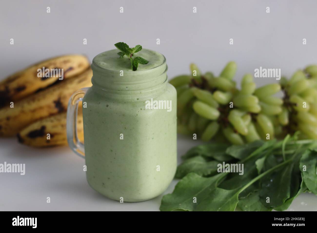 Smoothie vert à base de raisins verts congelés, jeunes épinards frais, bananes et lait d'amande. Servi dans un pot de maçon. Prise de vue sur fond blanc. Banque D'Images Smoothie vert à base de raisins verts congelés, jeunes épinards frais, bananes et lait d'amande. Servi dans un pot de maçon. Prise de vue sur fond blanc. Banque D'Images