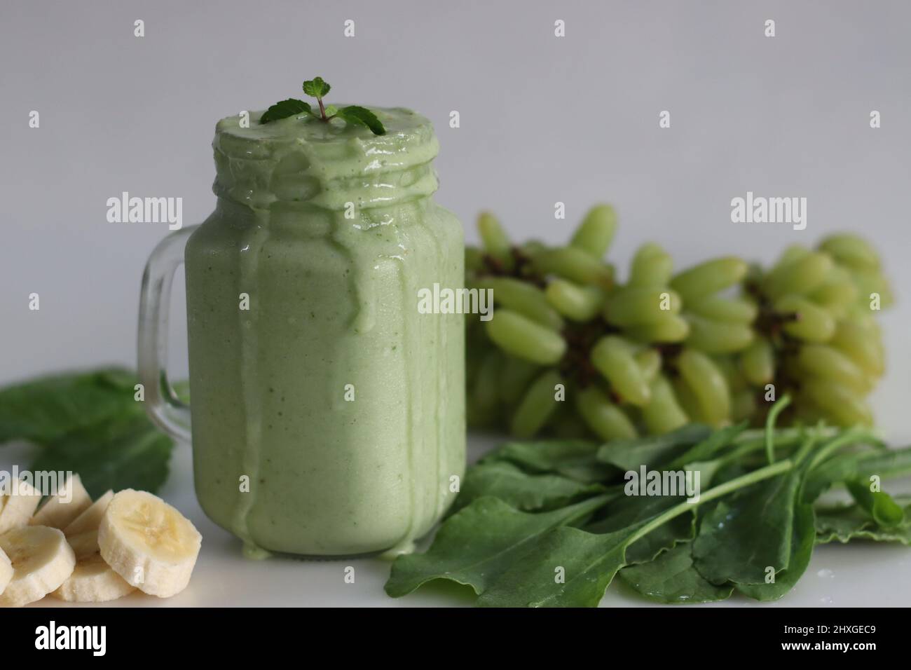 Smoothie vert à base de raisins verts congelés, jeunes épinards frais, bananes et lait d'amande. Servi dans un pot de maçon. Prise de vue sur fond blanc. Banque D'Images Smoothie vert à base de raisins verts congelés, jeunes épinards frais, bananes et lait d'amande. Servi dans un pot de maçon. Prise de vue sur fond blanc. Banque D'Images