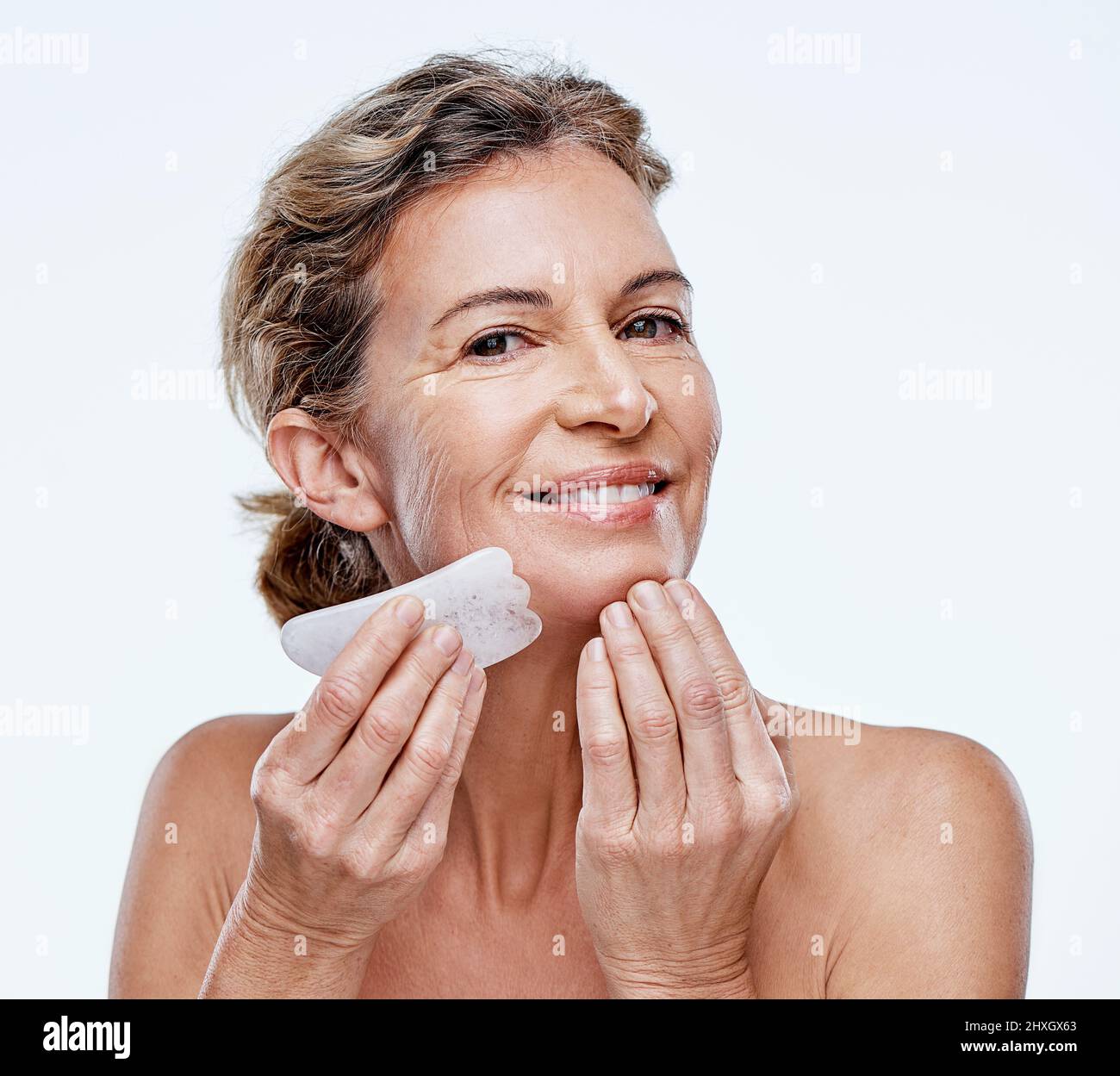 Cela fonctionne vraiment. Coupe courte d'une femme mûre utilisant une qua Sha sur son visage. Banque D'Images