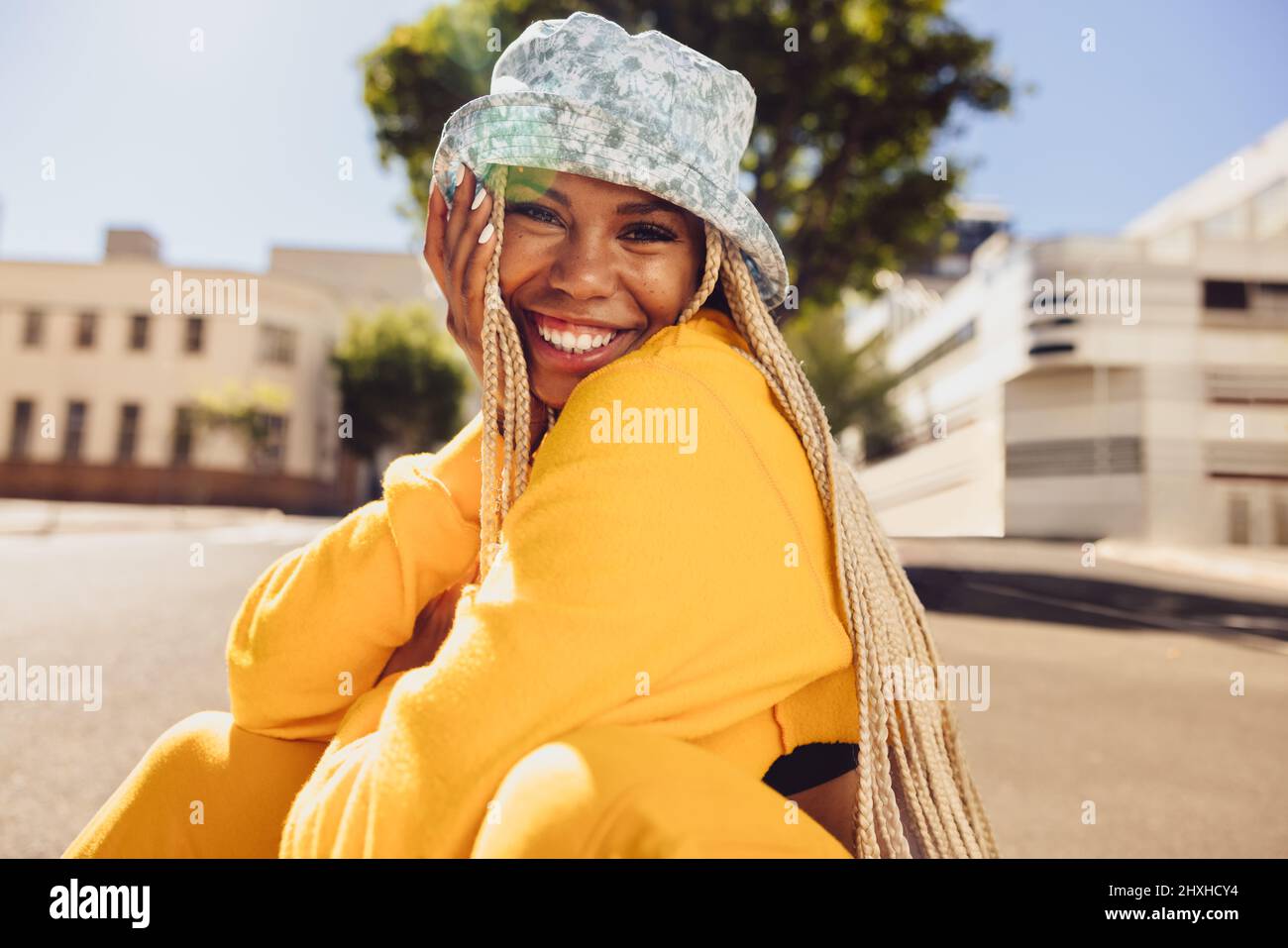 Jeune femme gaie souriant à l'appareil photo tout en étant assise à l'extérieur pendant un jour d'été. Bonne jeune femme s'amusant au soleil. Vêtements de jeune femme vibrants Banque D'Images