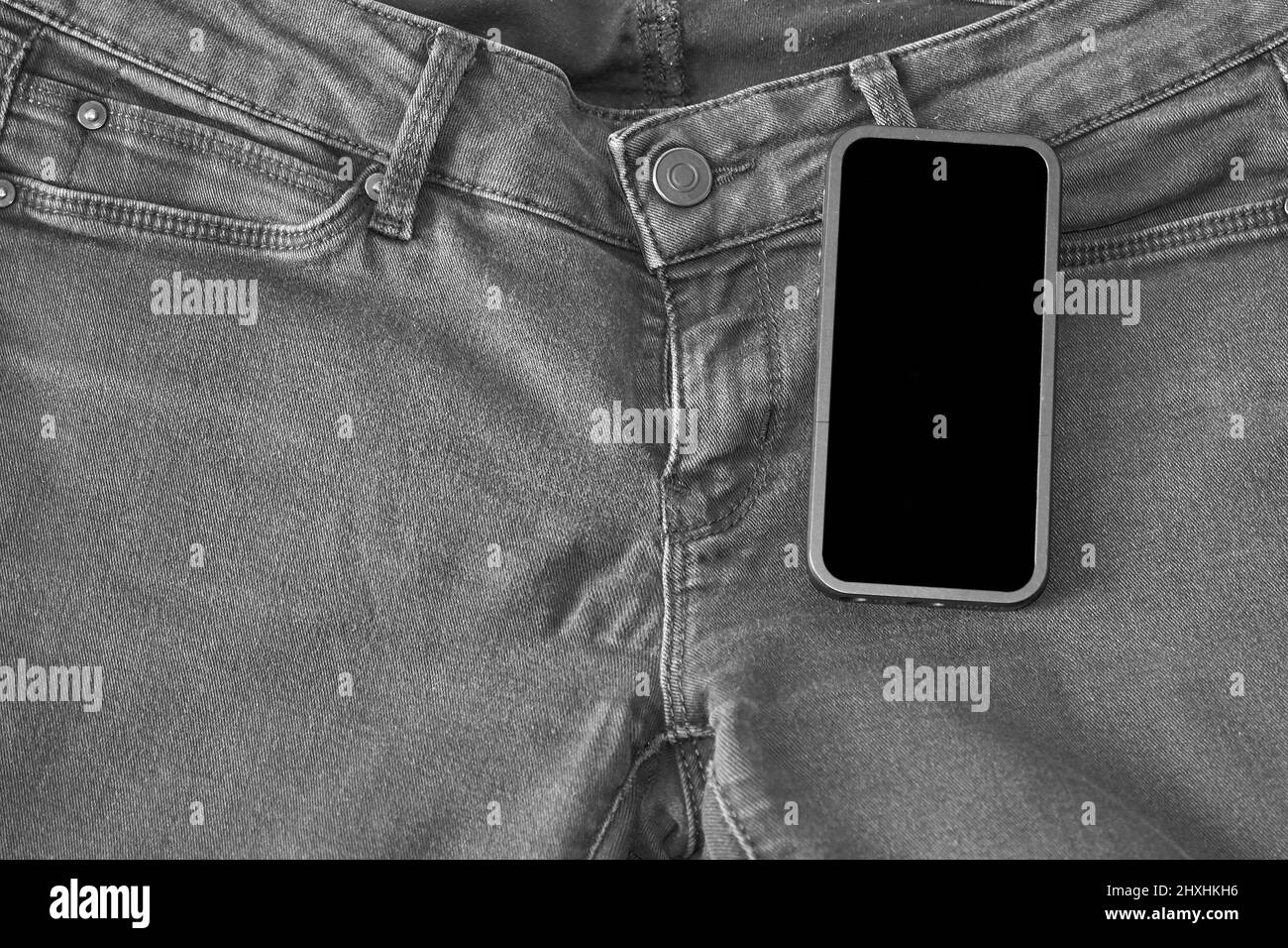 Partie supérieure d'un Jean noir ancien et d'un smartphone avec écran noir Banque D'Images