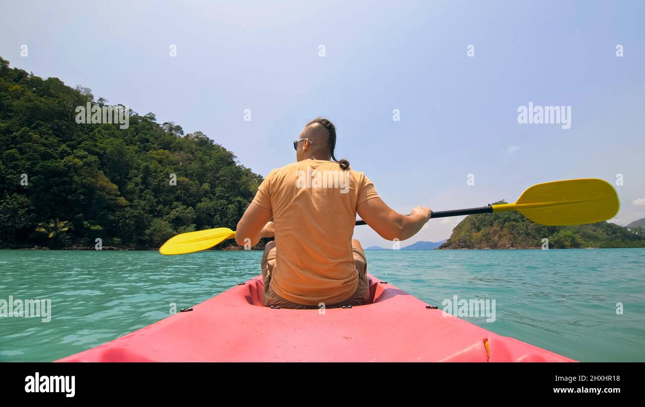 Jeune homme avec des lunettes de soleil et un chapeau rows en plastique rose canoë le long de la mer contre des îles vertes vallonnées avec des jungles sauvages. Voyager dans les pays tropicaux. St Banque D'Images