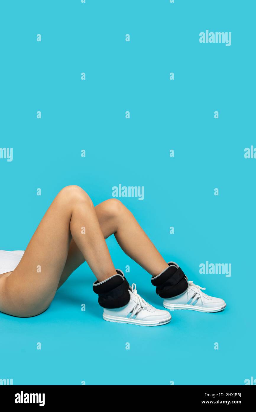 Gros plan des jambes de jeunes femmes ayant des baskets et un body blancs  avec des poids de poignet reposant sur un fond bleu faisant des exercices  physiques. En bonne santé Photo