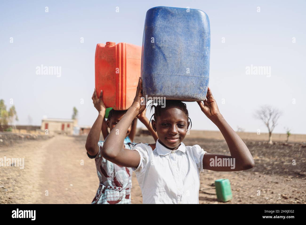 Deux filles africaines avec des bidons d'eau sur leur tête marchant dans un paysage stérile et désole ; pénurie d'eau et problèmes de changement climatique Banque D'Images