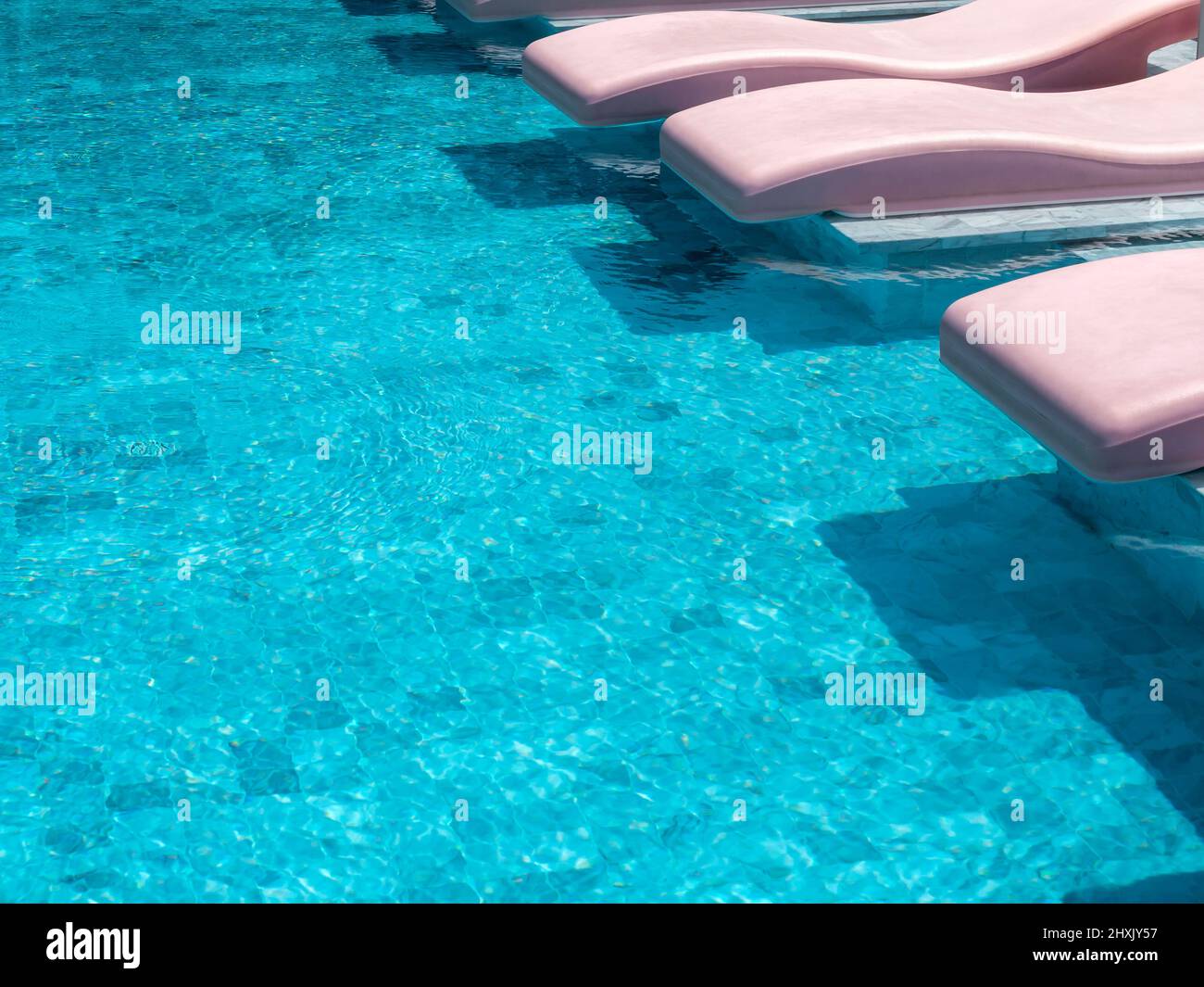 Le style rétro vide des chaises longues incurvées de couleur rose, des chaises sur la piscine bleue dans un hôtel de villégiature le jour ensoleillé, vacances d'été backgroun Banque D'Images
