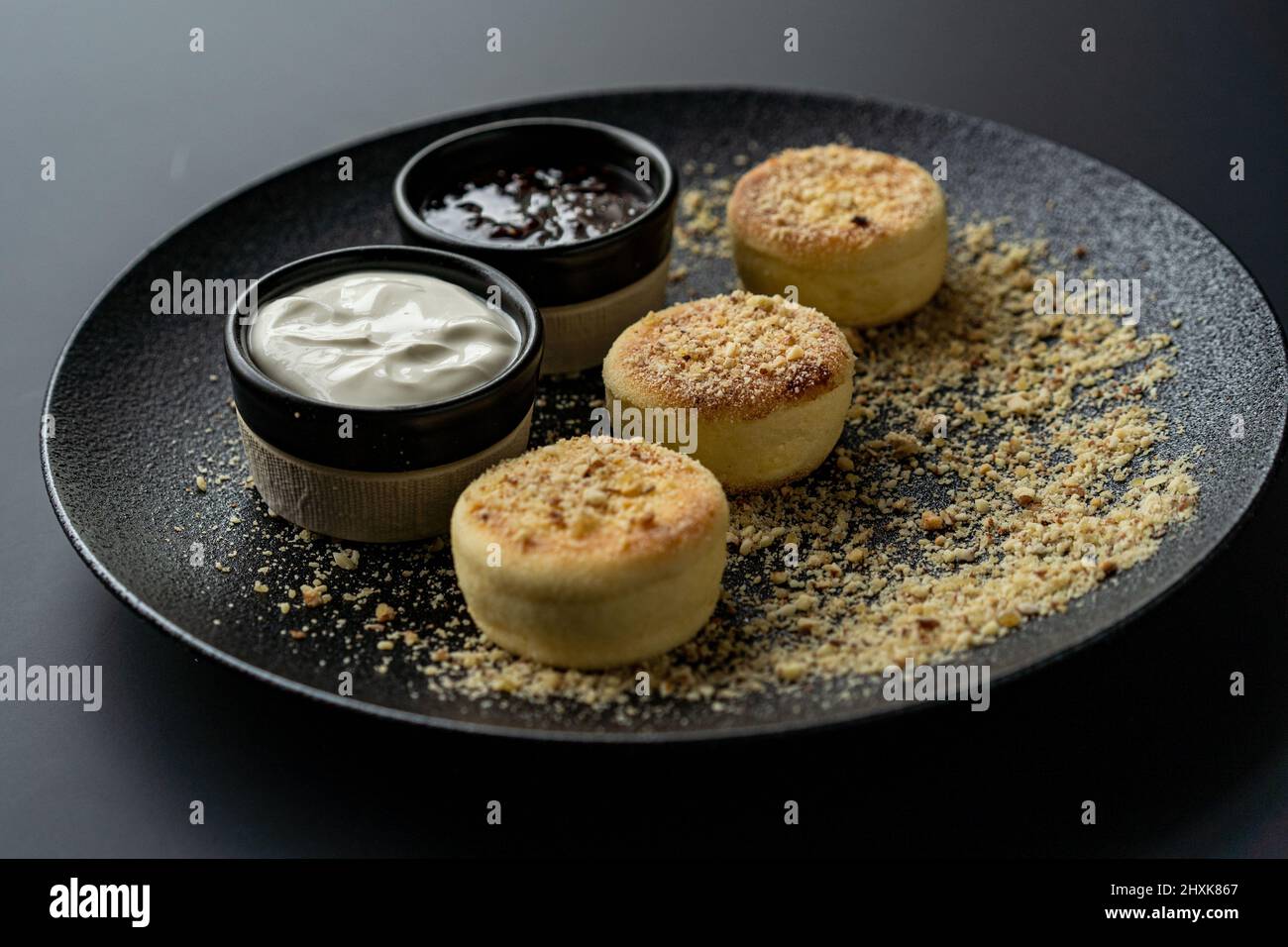 cheesecake au fromage cottage dans une assiette noire avec de la crème aigre et de la confiture Banque D'Images