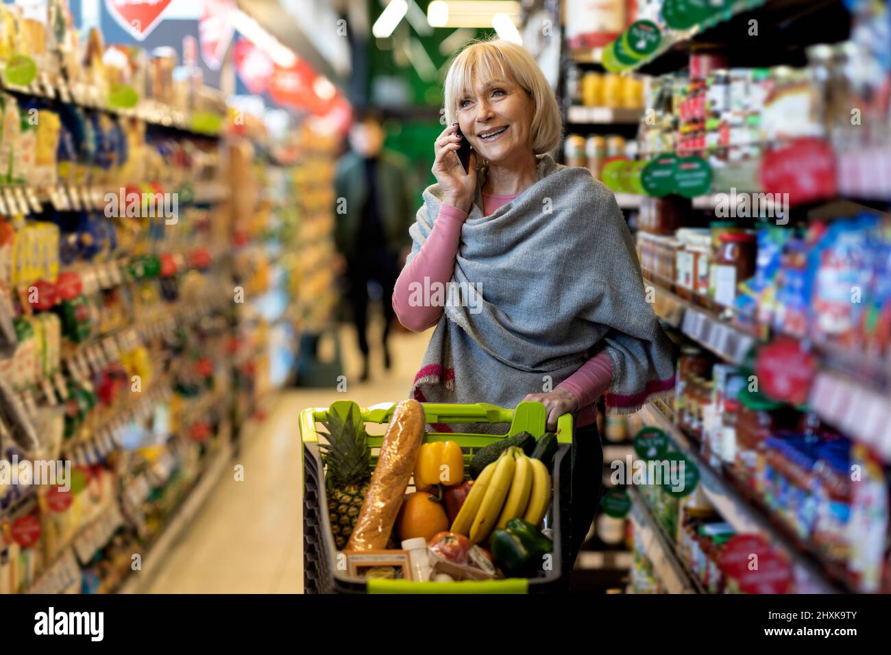 Femme âgée positive ayant une conversation téléphonique pendant le magasinage Banque D'Images