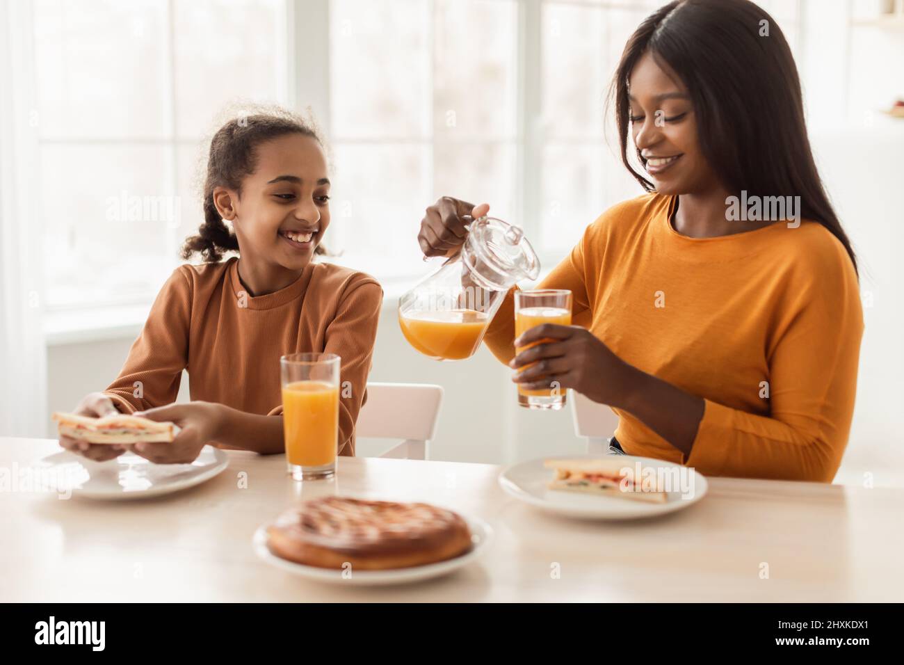 Joyeux Noir mère et fille boire du jus d'orange dans la cuisine Banque D'Images