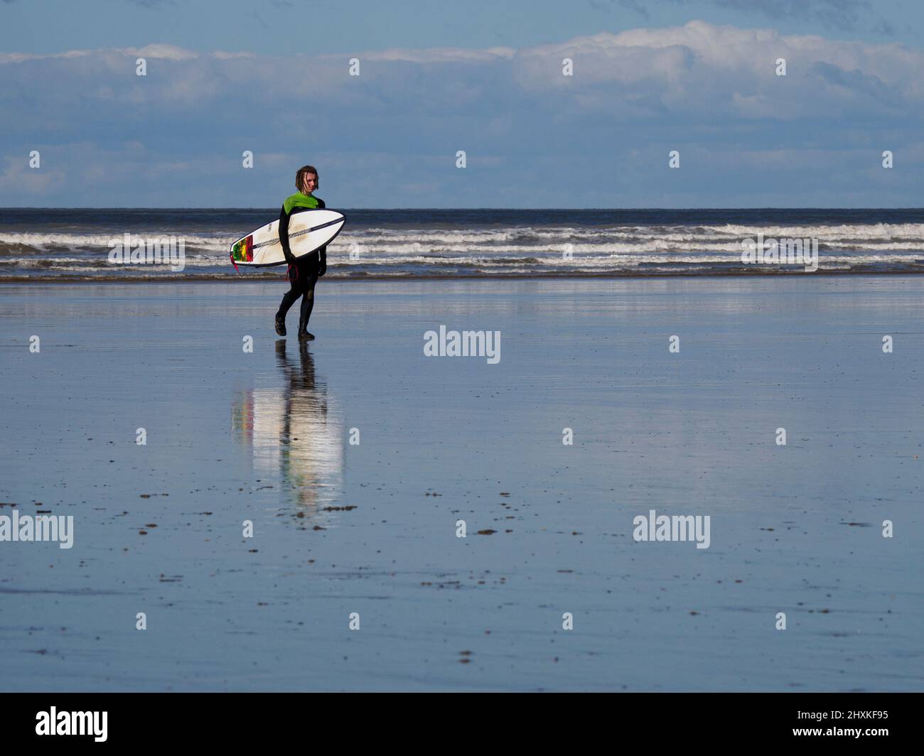 Jeune surfeur mâle adulte marchant sur la plage transportant des planches de surf, Westward Ho!, Devon, Royaume-Uni Banque D'Images