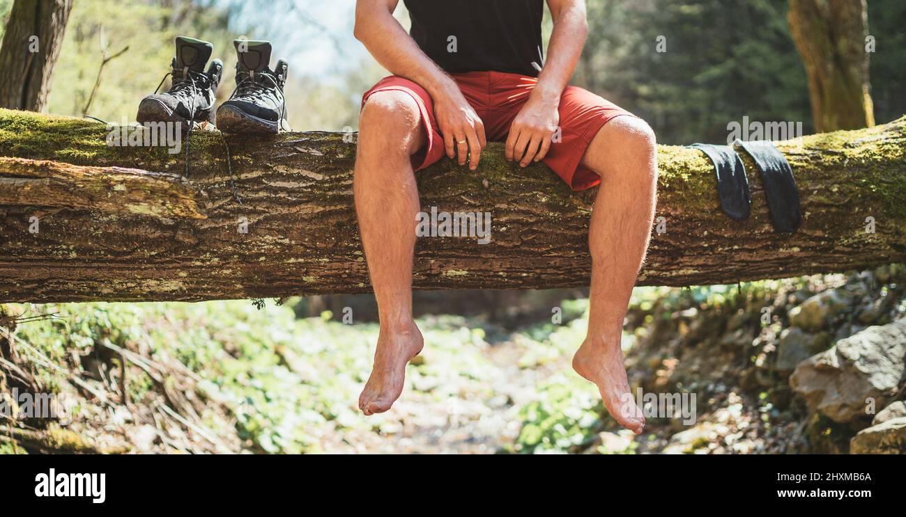 Homme assis sur une bûche d'arbre tombé au-dessus de la rivière de la forêt de montagne en attendant des chaussettes et trekking bottes séchage de blanchisserie. Personnes actives voyageant, Banque D'Images