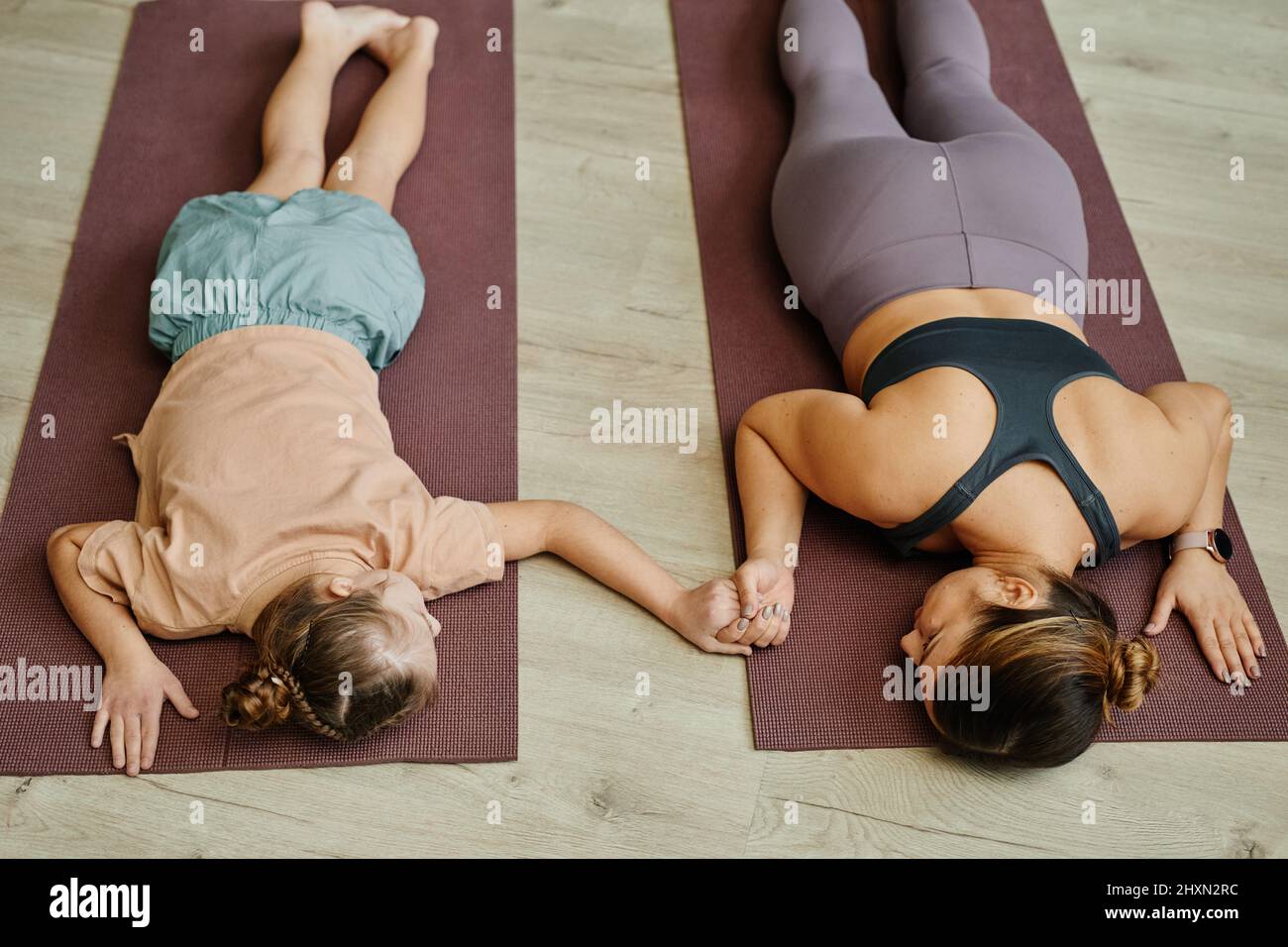 Vue de dessus de la jeune fille avec le syndrome de Down tenant les mains avec la mère ou l'instructeur tout en faisant des exercices sur les tapis de yoga à la maison Banque D'Images