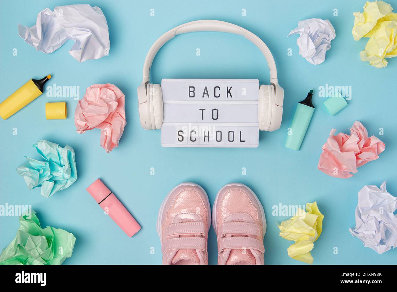 Texte de retour à l'école sur la visionneuse.Écouteurs, chaussures roses, boules de papier froissé de couleur, marqueur sur fond bleu.Concept d'éducation.Vue de dessus à plat Banque D'Images