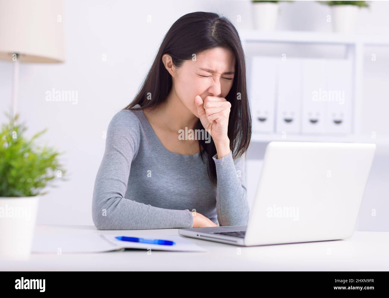 Une jeune femme malade qui s'occupe d'un ordinateur portable tousse lutte contre le coronavirus ou la grippe sur le lieu de travail Banque D'Images