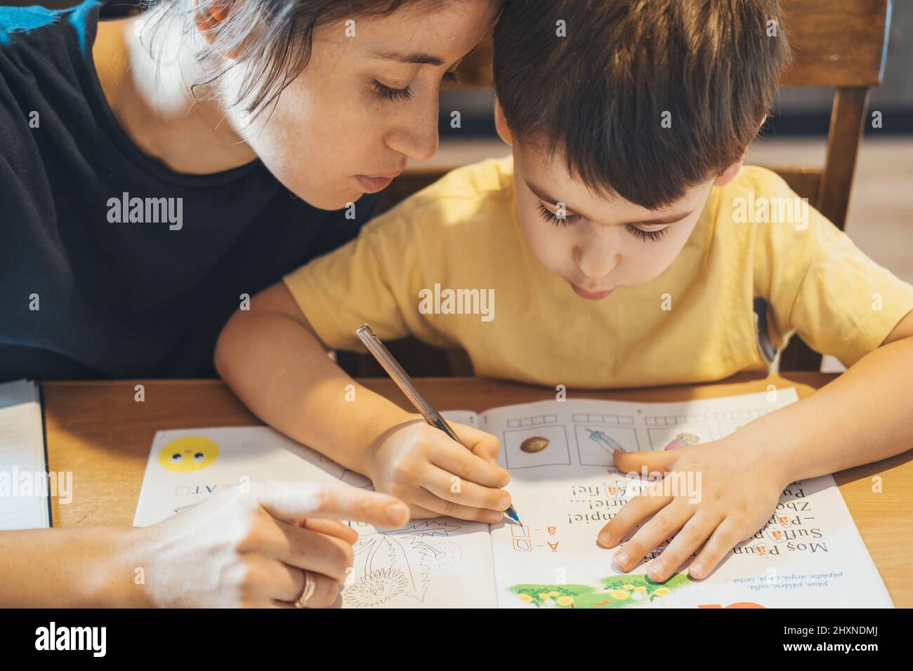 Portrait en gros plan d'une mère ciblée aidant le garçon à faire ses devoirs. Portrait pour un style de vie. Étudier, faire des devoirs. Éducation des enfants. Banque D'Images