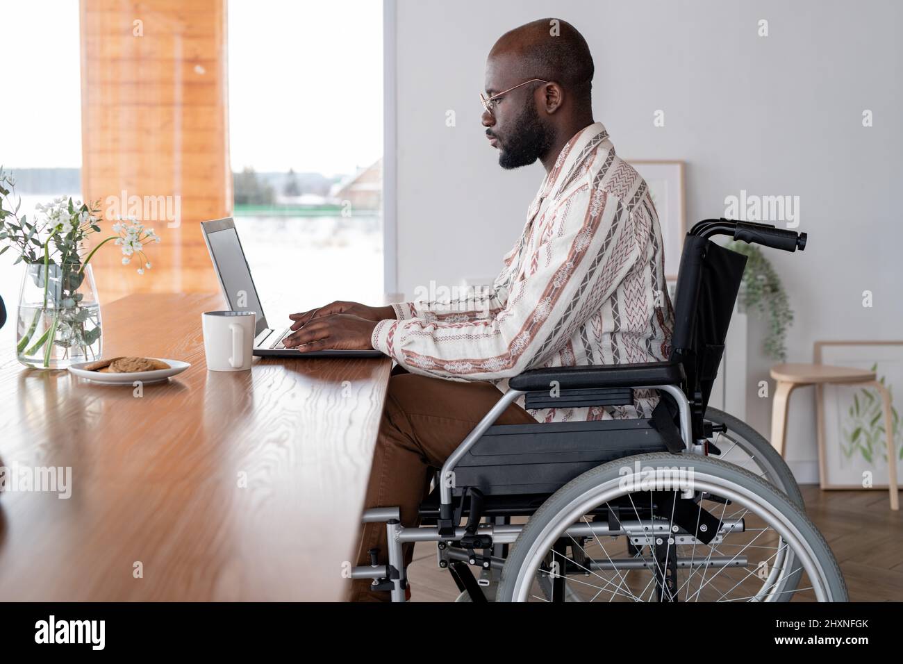 Vue latérale d'un homme noir sérieux travaillant sur Internet ou analysant des données en ligne assis devant un ordinateur portable près d'une table Banque D'Images