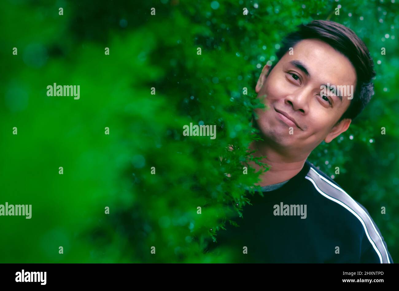 Homme asiatique souriant avec un visage heureux debout dans le Bush vert pour un bon concept de santé mentale. Banque D'Images