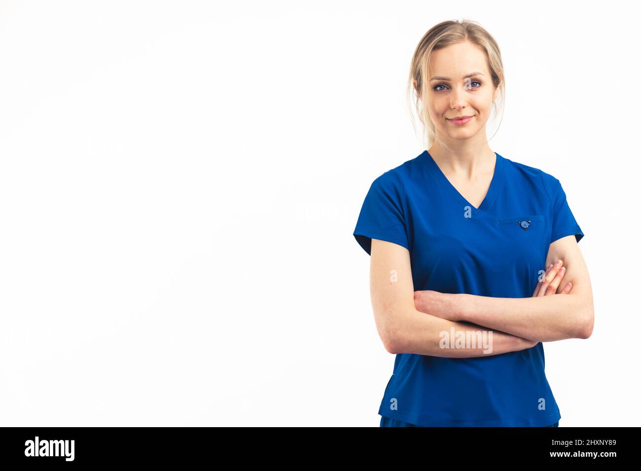 Femme blonde positive de soins de santé en uniforme bleu foncé regardant la caméra et croisant ses bras. Prise de vue en studio intermédiaire isolée. Photo de haute qualité Banque D'Images