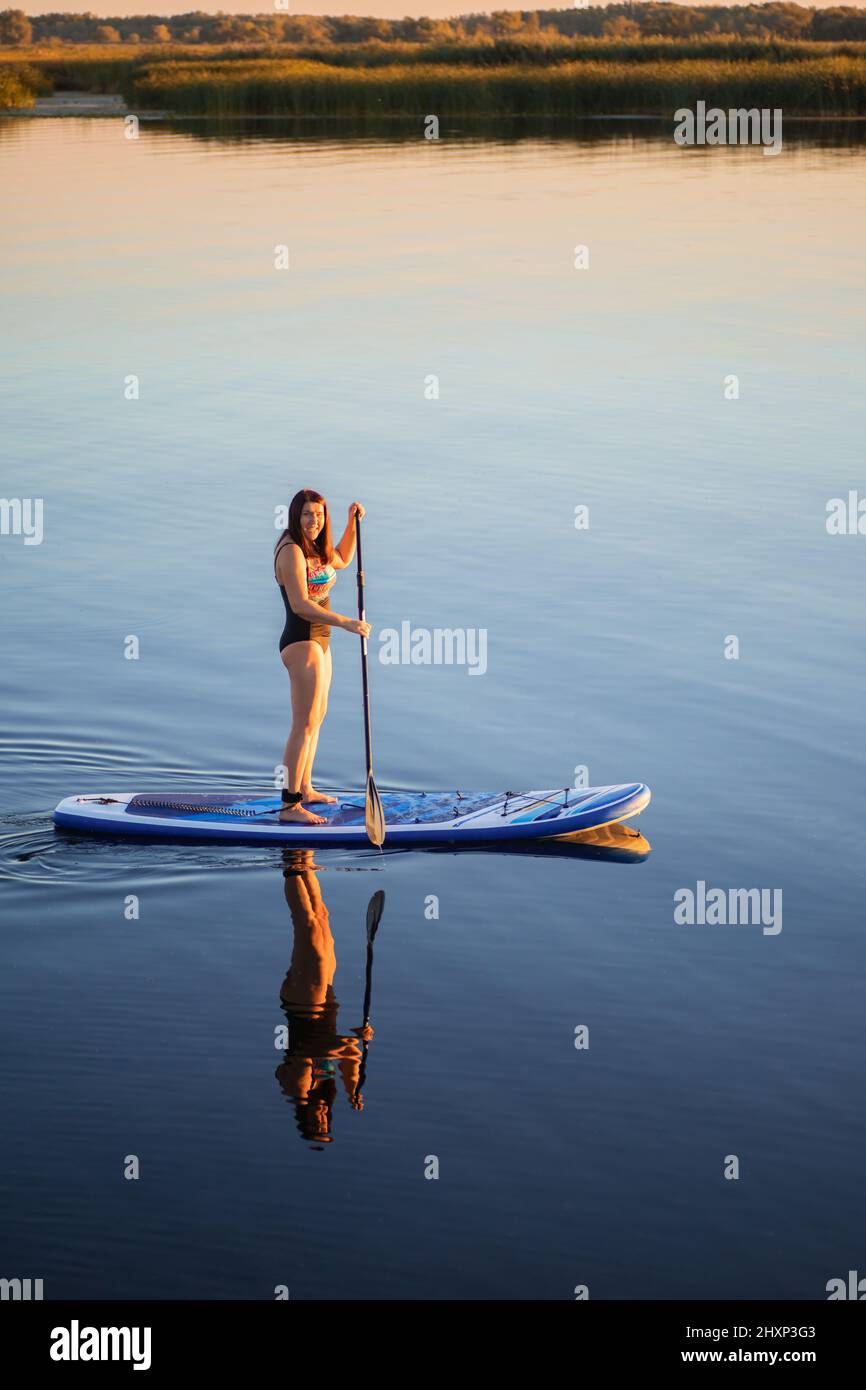 Portrait d'une femme caucasienne d'âge moyen qui s'embarque sur le lac le soir en été en regardant la caméra souriant avec des roseaux en arrière-plan Banque D'Images