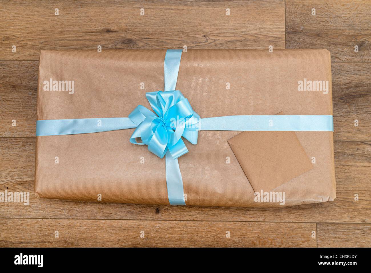 Un cadeau enveloppé de papier gris, enveloppé d'un ruban bleu attaché dans un noeud, allongé sur des panneaux en vinyle. Banque D'Images