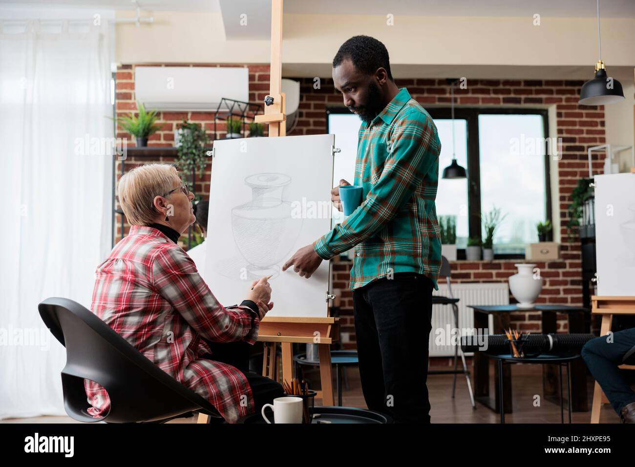 Professeur d'art afro-américain expliquant dessiner l'illustration à la femme senior travaillant ensemble à l'esquisse graphique dans le studio de créatination. Divers équipe dessin vase modèle sur toile apprentissage de nouvelles compétences artistiques Banque D'Images