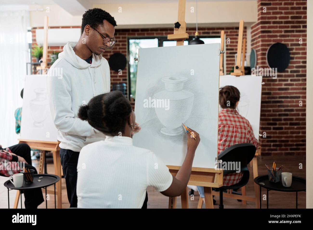 Professeur peintre expliquant la technique d'illustration à l'étudiant travaillant ensemble à la technique graphique pour le projct de l'école. Divers groupes d'artistes dessinant un modèle de vase sur toile blanche pendant la leçon d'art Banque D'Images