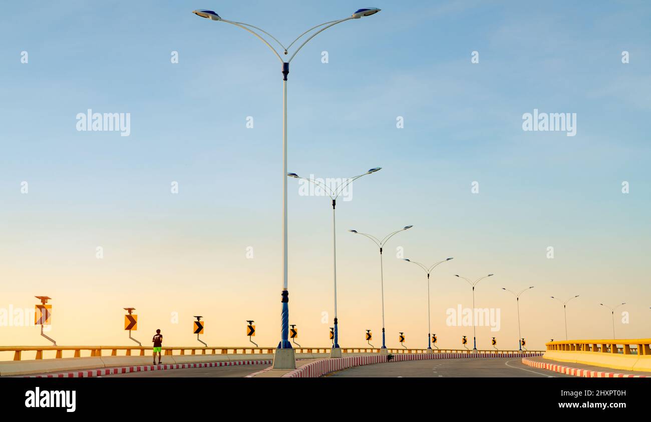 Route courbe avec lampadaire et panneau de signalisation jaune. Vue arrière d'un homme qui court sur un sentier à côté d'une route vide. Arrêt interdit rouge-blanc Banque D'Images