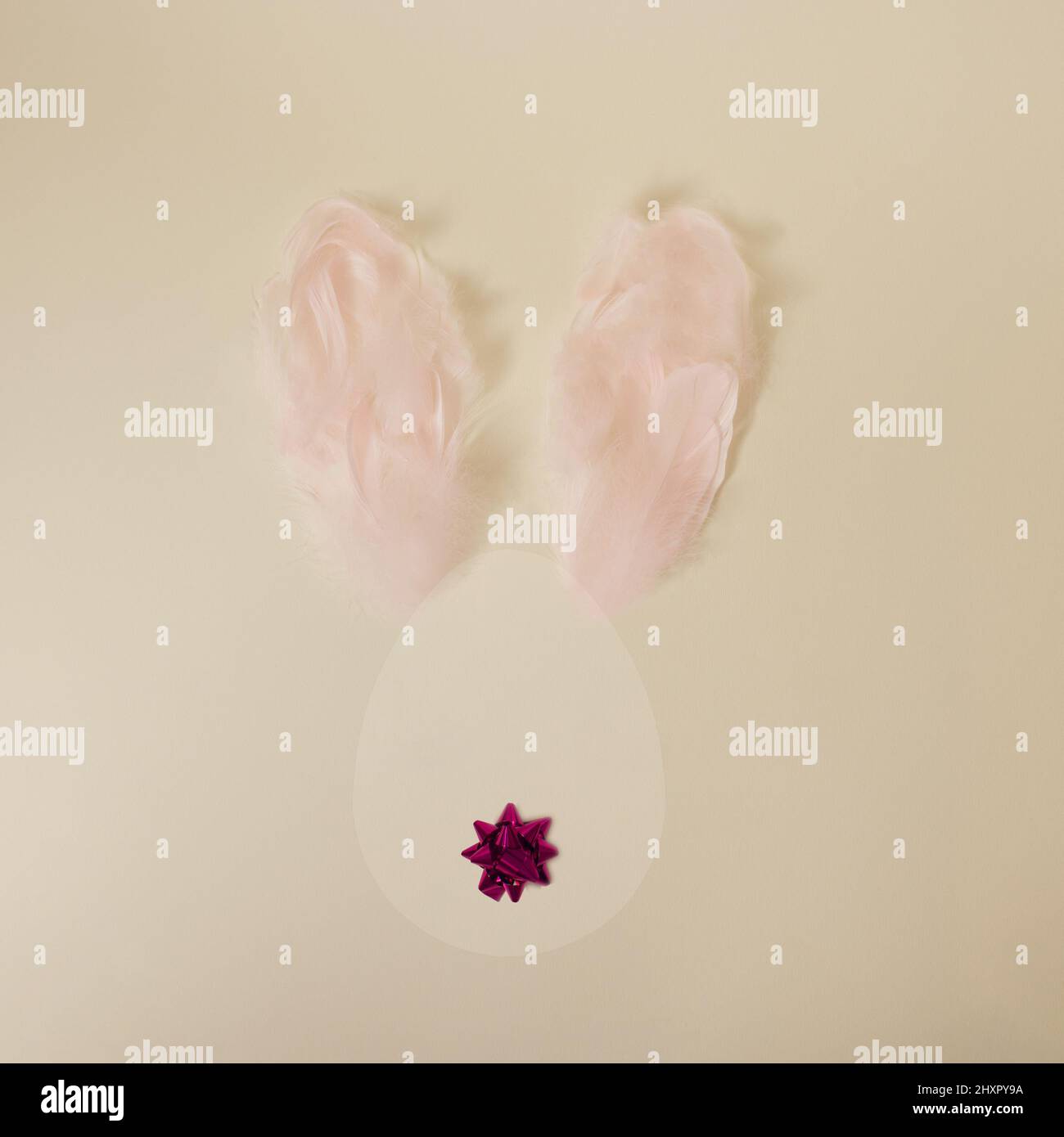 Joli lapin de Pâques en forme d'œuf avec des oreilles en plumes rose pastel et une queue d'arc décorative sur fond jaune minimal Banque D'Images
