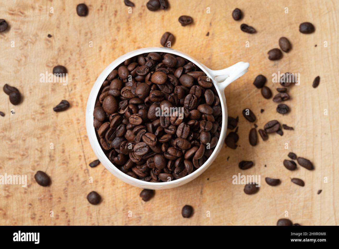 Vue de dessus d'une tasse de café blanc remplie de grains de café entiers sur une table en bois Banque D'Images