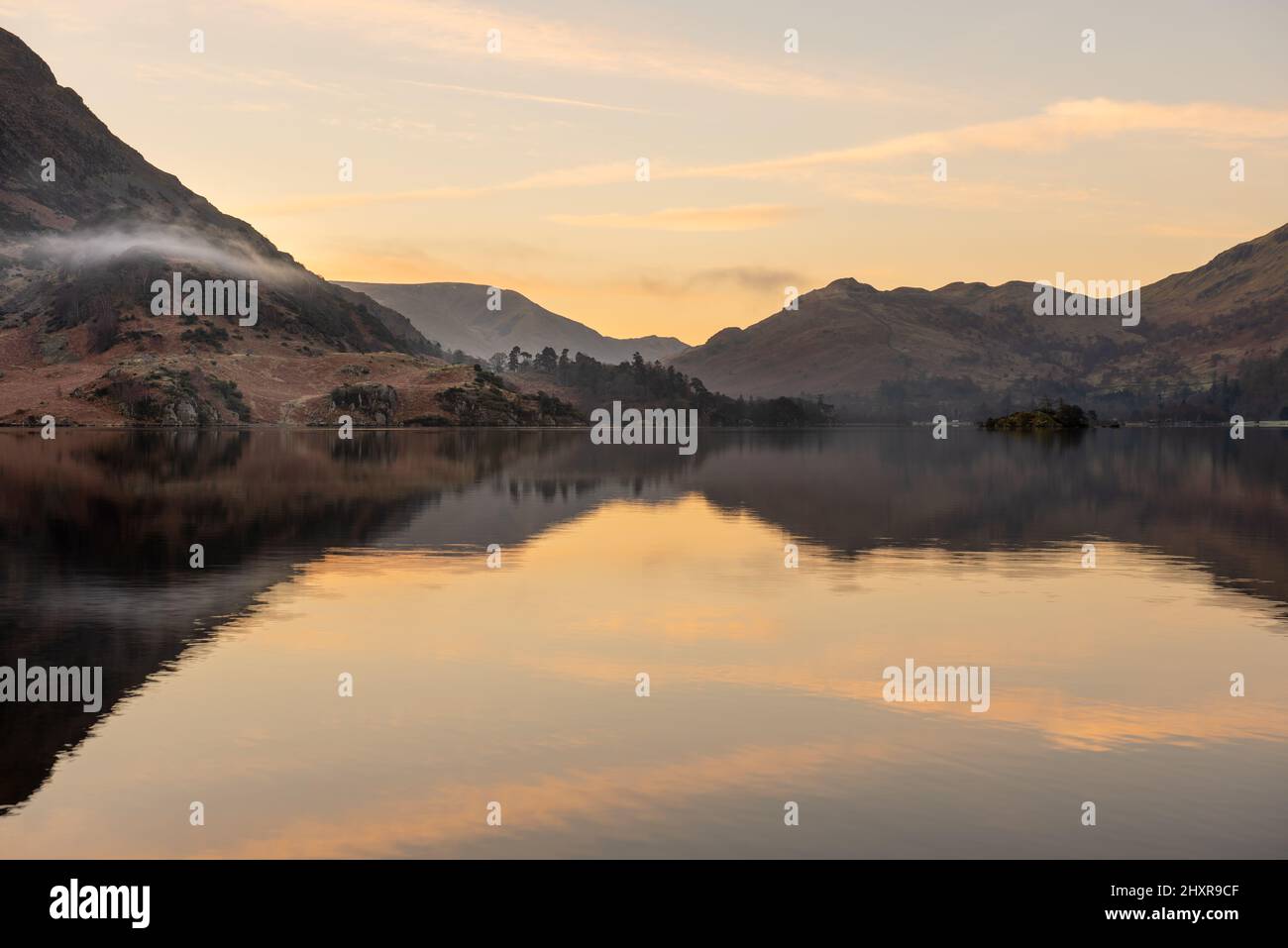 Lever de soleil paisible sur le lac avec des reflets calmes lors d'une belle matinée d'été. La brume roulante peut être vue qui persiste autour des montagnes. Cumbria. Banque D'Images