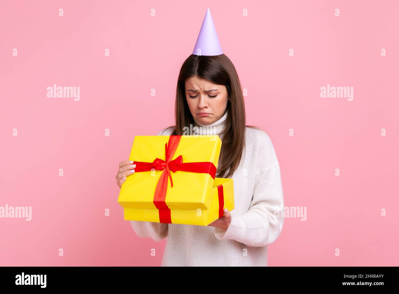 Déçue femme dans le cône de partie regardant à l'intérieur enveloppé boîte  cadeau, cadeau ouvert, surprise désagréable, portant blanc style  décontracté pull. Studio d'intérieur isolé sur fond rose Photo Stock - Alamy