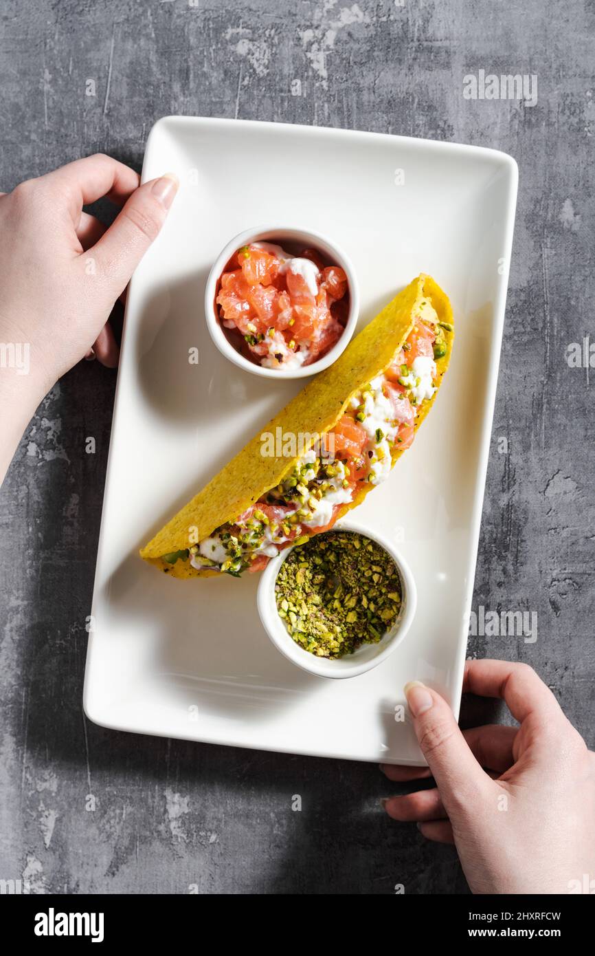 tacos au maïs avec saumon, mayonnaise et pistaches sur une table en béton et une main femelle Banque D'Images