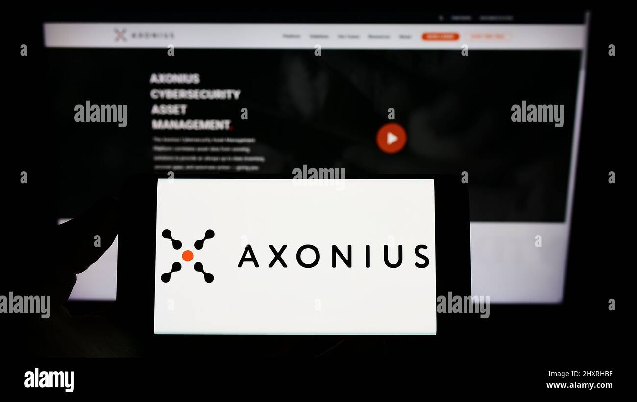 Personne tenant un téléphone portable avec le logo de la société américaine de cybersécurité Axonius Inc. À l'écran en face de la page Web d'affaires. Mise au point sur l'affichage du téléphone. Banque D'Images