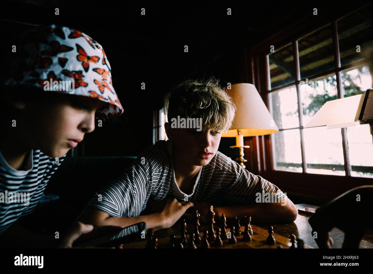 Les garçons jouent ensemble aux échecs dans une cabine rustique à la lumière de la fenêtre Banque D'Images