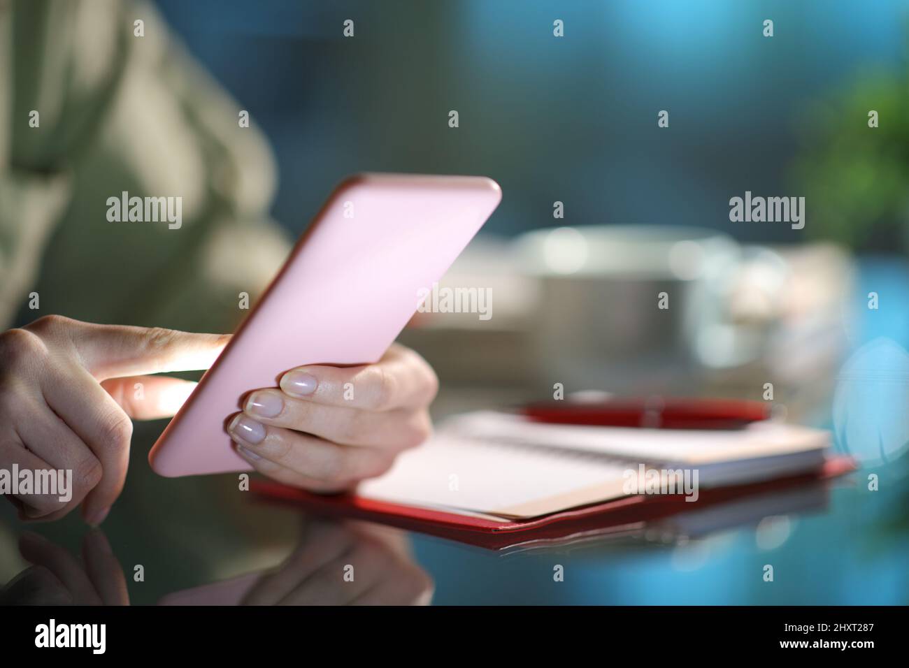 Gros plan d'une main de femme utilisant un smartphone à côté de l'agenda dans un bureau dans la nuit à la maison Banque D'Images