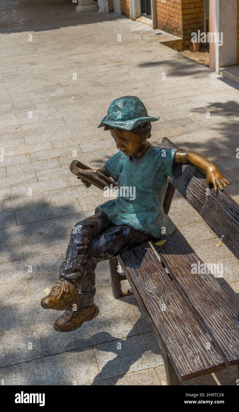 Photo verticale d'un monument en bronze d'un garçon lisant sur le banc en Thaïlande Banque D'Images