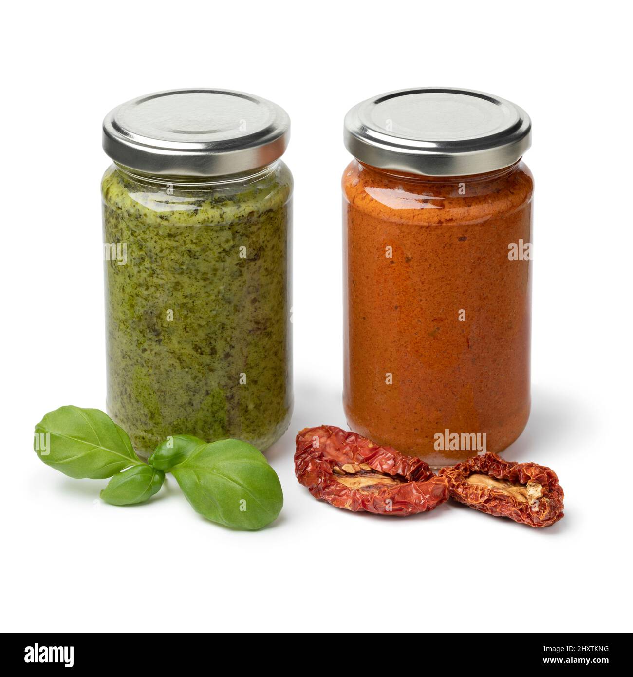 Bocal en verre avec pesto italien rouge et vert avec tomates douces séchées et feuilles de basilic frais à l'avant isolées sur fond blanc Banque D'Images