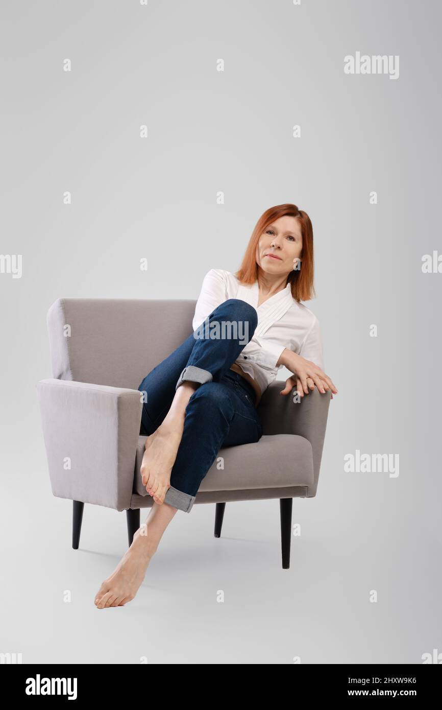 Femme d'âge moyen se détendre dans un fauteuil confortable. Studio concept de vie sans souci. Banque D'Images