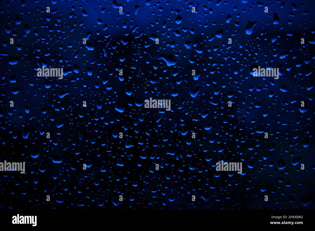 La pluie d'eau tombe sur une surface bleu profond comme arrière-plan. Toile de fond abstraite. Banque D'Images