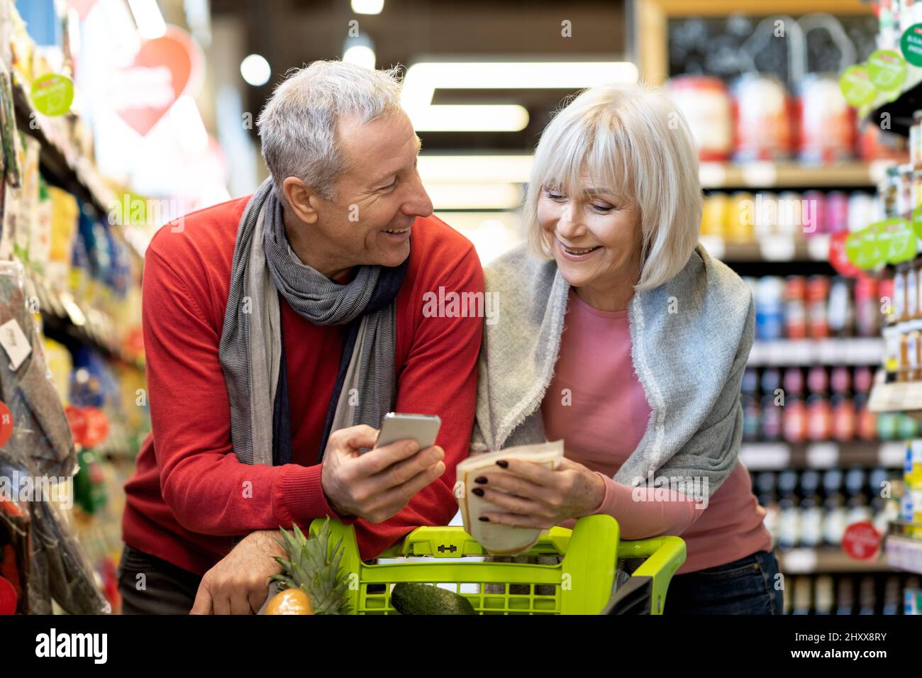 Un mari et une femme âgés heureux magasinent ensemble, à l'aide d'un smartphone Banque D'Images