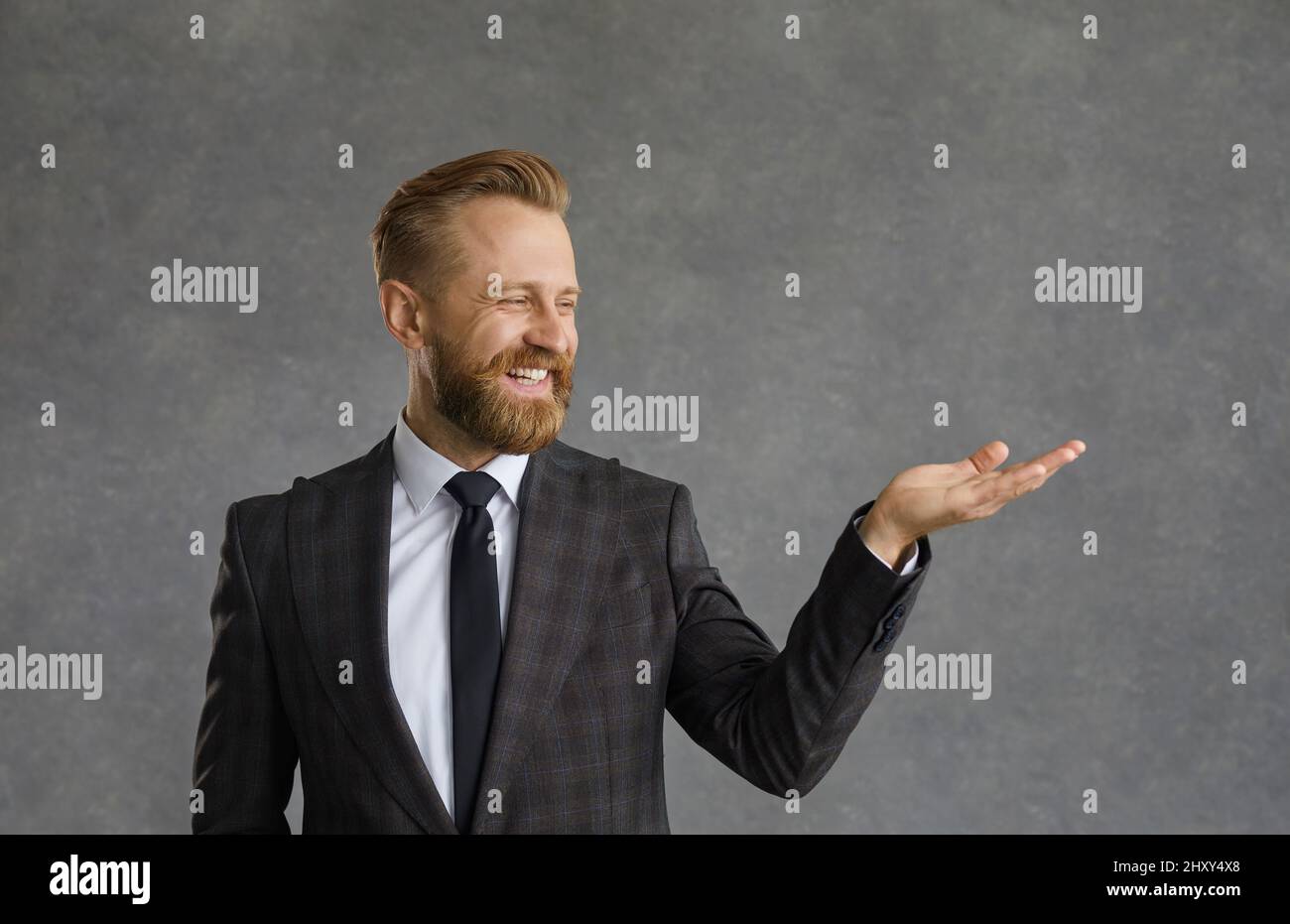Un bel homme barbu dans une chemise blanche et une veste noire avec un sourire démontre un produit imaginaire Banque D'Images