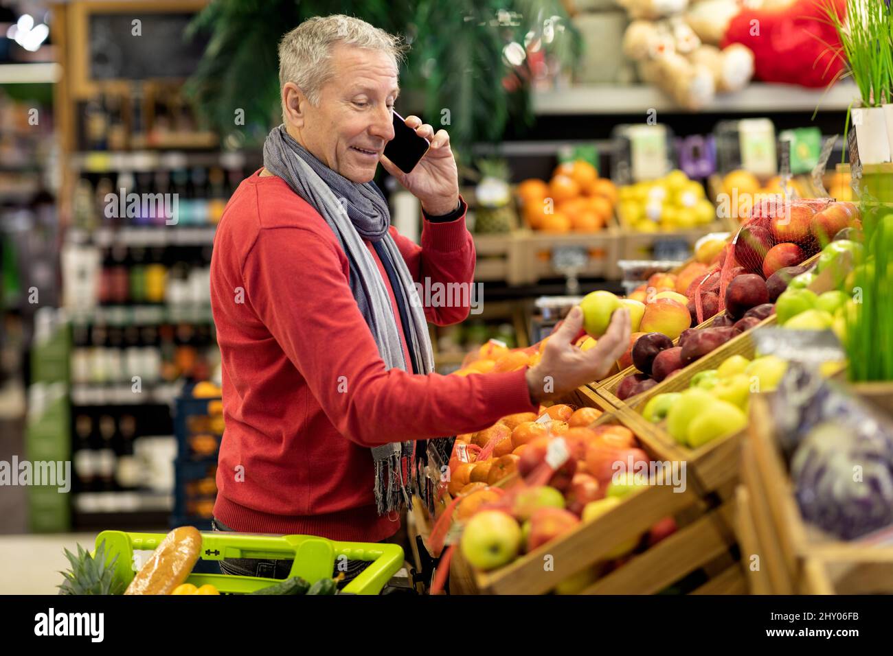 Beau homme senior ayant une conversation téléphonique pendant le magasinage Banque D'Images