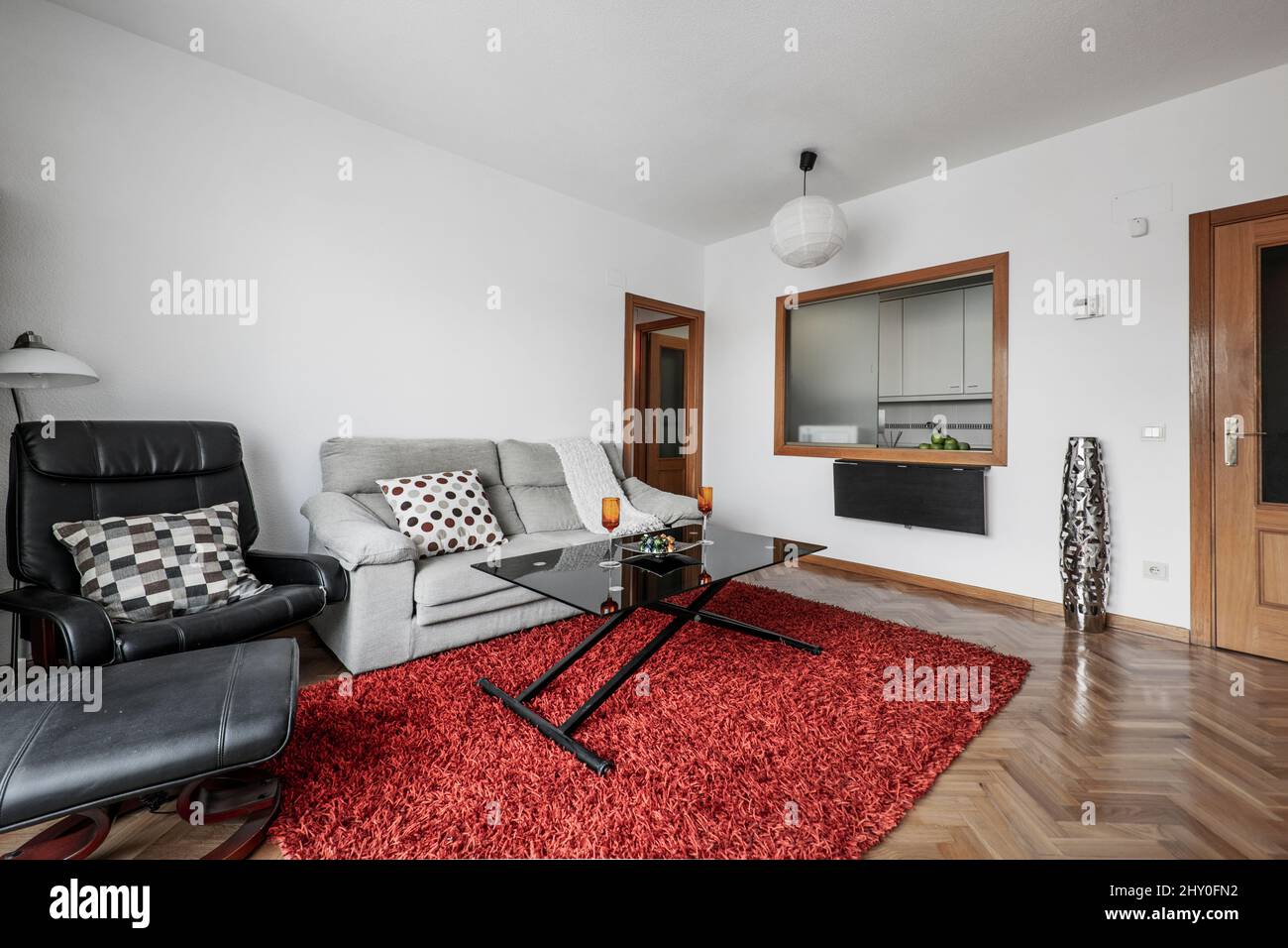 Salon de location de vacances avec moquette rouge, canapé 2 places gris et  chaise de massage noire avec table en verre noir Photo Stock - Alamy